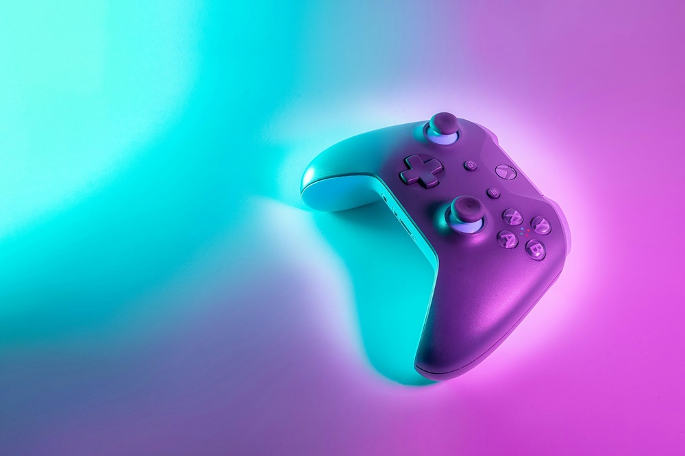 A video game controller is illuminated by blue and pink neon lights, creating a vibrant, colourful gradient background.