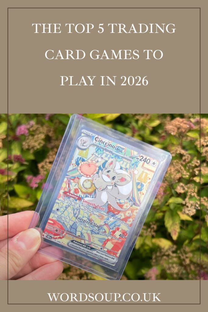 A hand holds a colourful trading card in a plastic sleeve against a leafy outdoor background. Text above reads, The Top 5 Trading Card Games to Play in 2026. Website wordsoup.co.uk is at the bottom.