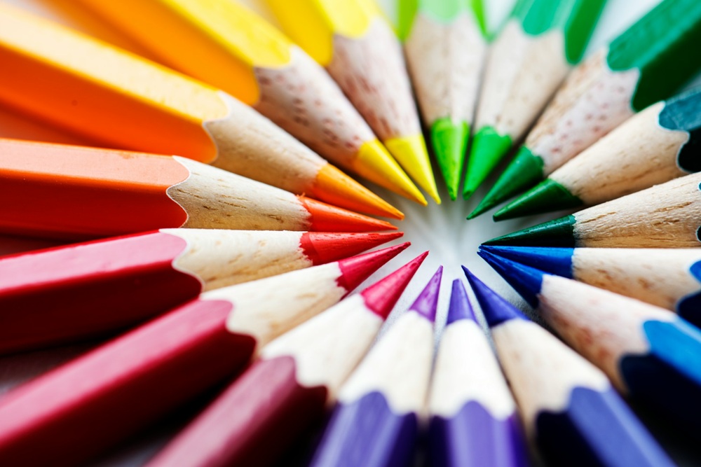 A close-up of coloured pencils arranged in a tight circle with their sharpened tips pointing inward, showcasing a vibrant spectrum of colours.
